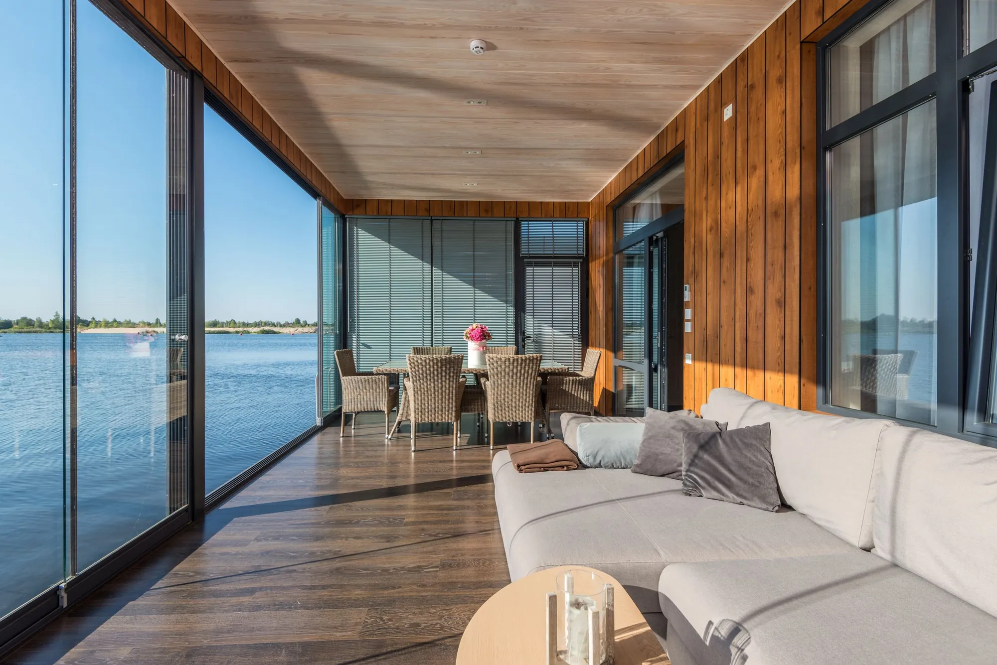 Sala com janelas de vidro do piso ao teto e vista para a água, recebendo sol direto